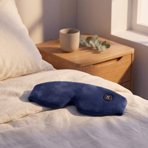 Cordless heated eye mask resting on the bed by a window