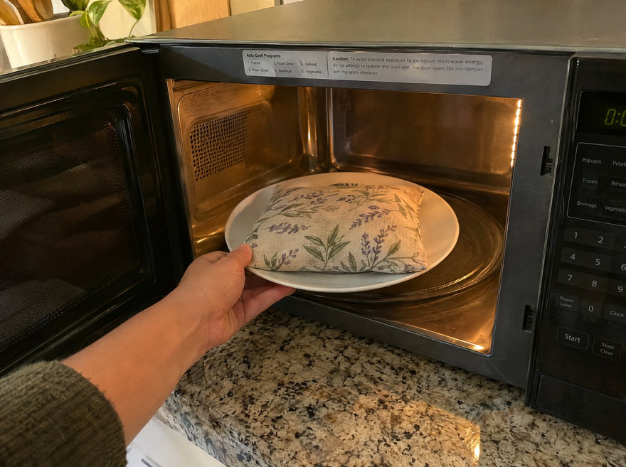 A hand placing a fabric heat pack on a plate into an open microwave
